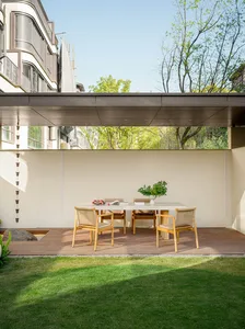 Modern terrace featuring a wooden table with a vase of flowers, surrounded by greenery and a wooden deck, with a gravel pathw