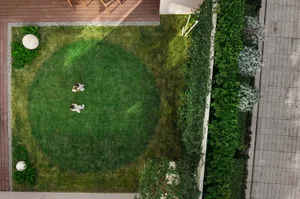 Two people walking on a round green lawn surrounded by greenery.