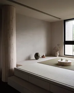 A minimalist living room featuring wooden furniture, a tatami mat, and a small tea set on a wooden platform.