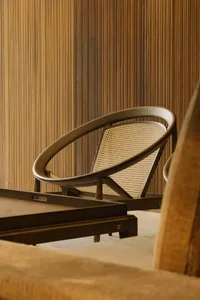 A modern circle wooden armchair with a woven seat against a striped wooden wall.