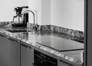 A modern minimalist kitchen featuring a marble countertop with a stainless steel sink and faucet, alongside a black coffee ma