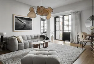 A modern minimalist living room with a fabric sofa, wooden coffee table, and glass windows.