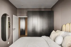 A minimalist bedroom featuring a bed with soft fabric bedding, a tufted wooden headboard, and a black cabinet.