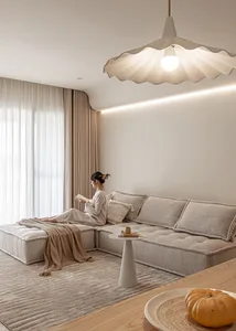 A minimalist living room featuring a monochromatic fabric sofa, modern light fixture, and large windows with sheer curtains.
