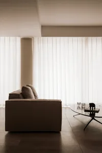 A minimalist living room with a brown upholstered sofa and white sheer curtains on the window, creating a serene and modern a