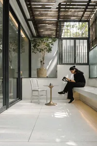 A minimalist living space with a concrete floor, a white chair, a small table with an object, and a potted plant.
