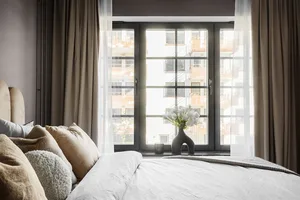 Modern bedroom with fabric bedding, white walls, and large window with curtains.