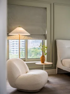 A modern bedroom featuring white upholstered furniture, a floor lamp, and a small round table with a vase containing greenery