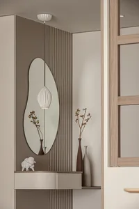 A modern entryway featuring a frameless oval mirror, a white pendant light, and decorative vases.
