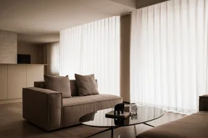 Modern living room featuring a fabric cushioned sofa with large windows and sheer curtains.