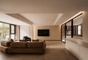 A modern minimalist living room with a concrete floor, brown leather sofa, and a large flat-screen TV mounted on the wall.