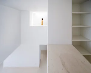 A minimalist interior with concrete walls and floor, featuring a solitary figure in a window.