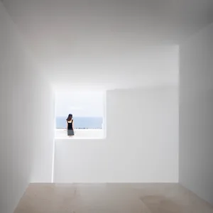 A minimalist white interior space with a concrete floor and a window overlooking a coastal view.