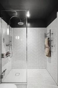 Modern bathroom with white tiled walls and floor, a glass shower enclosure, and minimalist design.