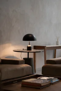 A modern living room featuring a round marble table with a black lamp, two plush brown sofas, and coffee table with books.