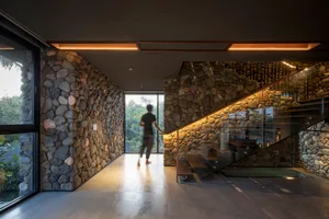 A modern staircase featuring stone walls and glass railings under warm, ambient lighting.