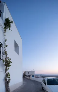 A modern white townhouse with a window box and a car parked nearby on a quiet street.