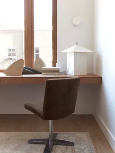 A minimalist home office featuring a wooden desk with books and a modern lamp.