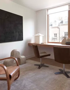 A modern home office featuring a sleek desk, stylish chairs, and a large window with a view of the outside.