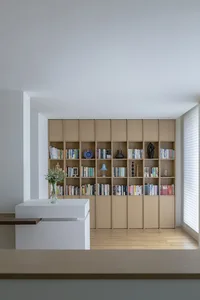 A modern living room with a wooden and glass bookshelf filled with books and decorative items.