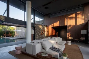 A modern living room with a natural stone accent wall and a large sofa in front of a large windows.