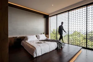 A modern minimalist bedroom with a concrete backdrop, featuring a large bed with white bedding and a wooden floor.