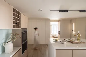 A modern minimalist kitchen with neutral-toned cabinetry and a kitchen island with a cutting board, wine bottle, and glass.