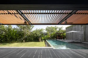 Modern residential patio featuring a wooden pergola, concrete walls, and lush greenery around a pool area.