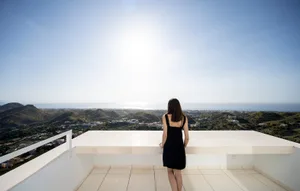 A woman standing on a modern terrace overlooking a scenic view of hills and the sea.