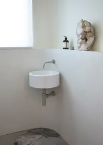 A minimalist modern bathroom with a circular sink, marble sculpture, and bottle of liquid.