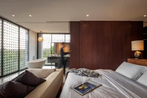Modern bedroom featuring a white bed and a brown wooden accent wall, with a white bathtub visible through the glass partition