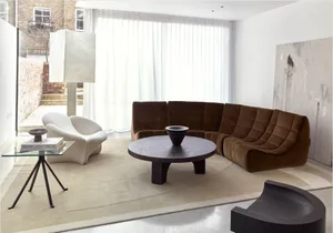 Modern living room featuring a sleek, brown velvet sofa and a round stone coffee table in a minimalist interior design settin