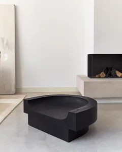 A sleek, black, modern minimalist concrete coffee table with a contoured edge sits in a bright, minimalist interior space.