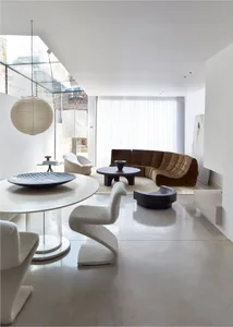 A minimalist living room with white walls, a curved sofa, a round table, and white chairs.