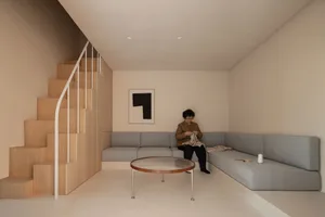 A minimalist living room featuring a grey fabric sofa, a modern coffee table, and a wooden staircase.