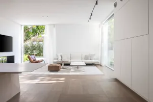 Modern minimalist living room featuring light wood flooring, marble coffee tables, and leather accent chair.