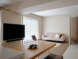 A minimalistic living room with light-colored walls, a white couch, and a wooden table.