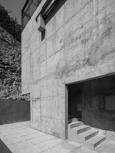 Modern concrete building facade with steps leading into a dark interior.