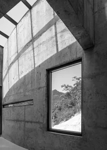 A modern interior space featuring concrete walls with a window showcasing a natural landscape.