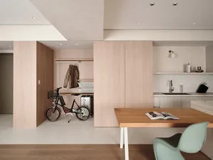 A modern, minimalist kitchen with wooden cabinets, a wooden dining table, and a bicycle in the background.