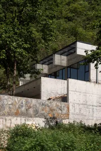 A modern minimalist home with concrete exterior and large windows overlooking a lush green hillside.