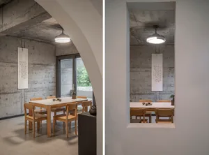 A modern minimalist dining room with concrete walls, wooden furniture, and a ceiling fan.