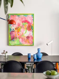 A vibrant abstract painting on a white wall above a dining room table with black chairs.