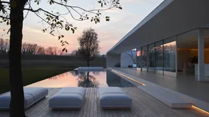 Modern house with glass walls and concrete patio during sunset.