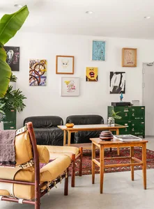 A modern living room featuring black leather sofas, wooden tables, and a collection of framed art on the wall.