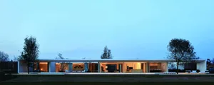 Modern residential exterior with glass and concrete materials, illuminated at dusk.