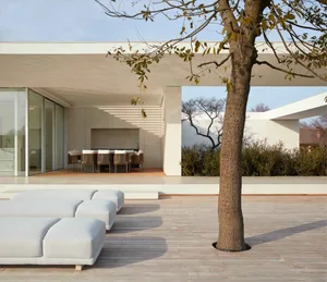 Modern residential outdoor area featuring white and minimalist design, concrete floor, wooden tree trunk, and outdoor furnitu