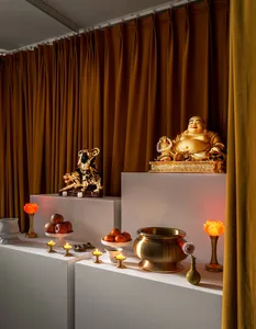 A religious altar with a golden Buddha statue, a statue of a deity on a tiger, various fruits, lit candles, and decorative it