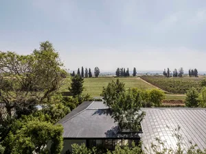 A metal-roofed farmhouse surrounded by lush green fields and trees under a clear sky.