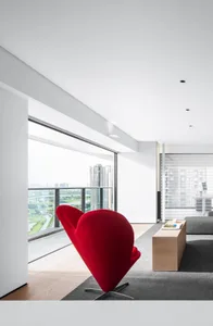 A modern living room featuring a striking red cone-shaped chair with a cityscape view through the floor-to-ceiling windows.